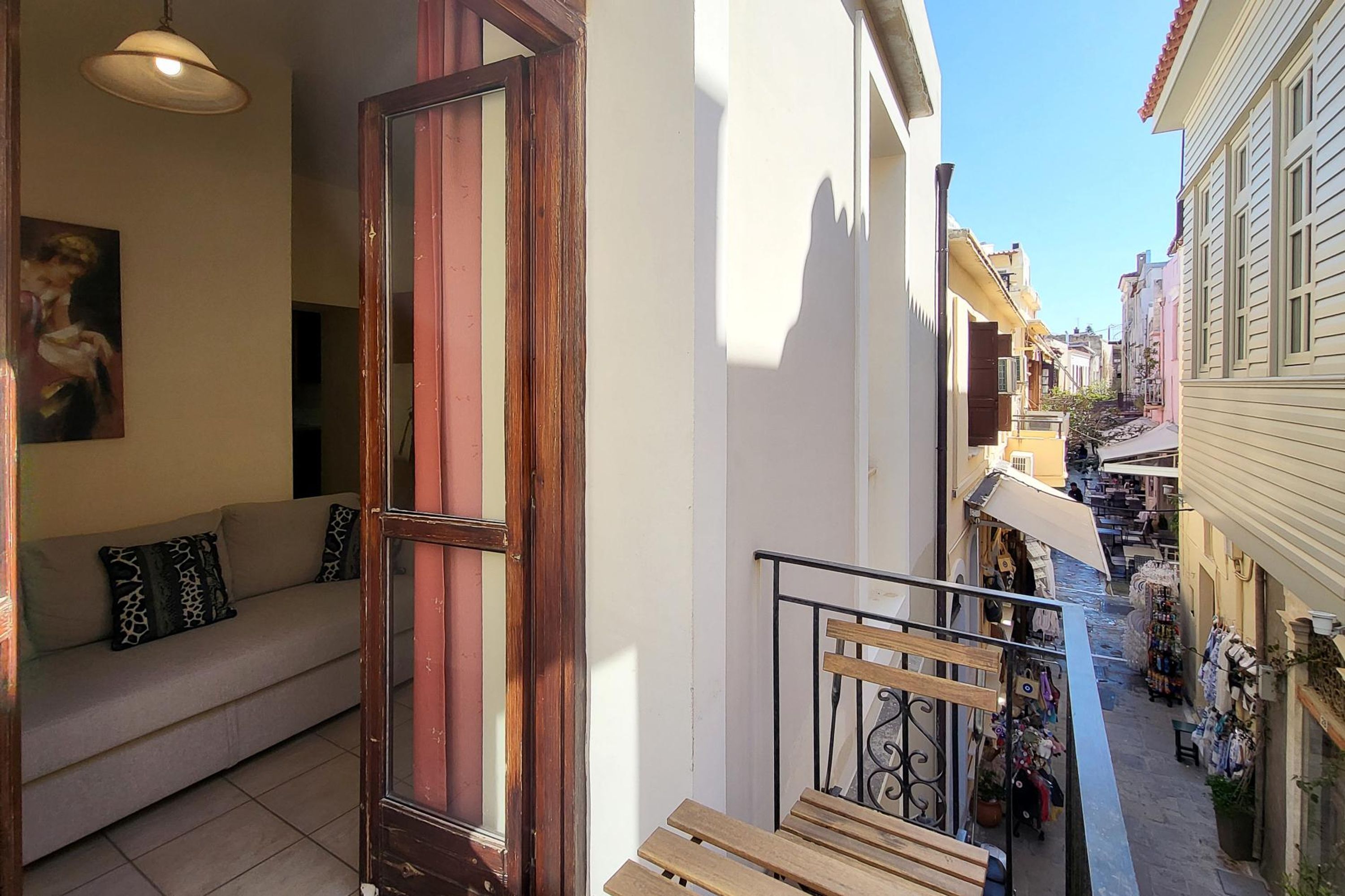 Une rue étroite, bordée de bâtiments des deux côtés, un banc en bois et un canapé avec des coussins à motifs.