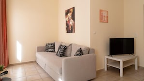 A living room with a grey sofa, patterned cushions, a flat-screen TV on a white stand, and a painting on the wall. - Katrina Superior Studio 4 With Balcony (Rethymno)
