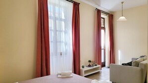 A hotel room with a bed, a sofa, a small table with a plant, and a window with curtains. - Katrina Superior Studio 4 With Balcony (Rethymno)