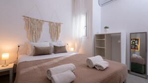 Ein ordentlich bezogenes Bett mit aufgerollten Handtüchern, einer Nachttischlampe und einem Wandbehang aus Makramee.