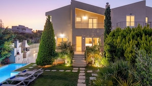 A modern two-story house with a swimming pool, outdoor seating, and a well-maintained garden.