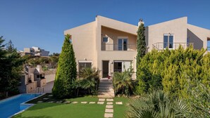 A modern two-story house with a swimming pool, a well-maintained lawn, and a variety of trees.