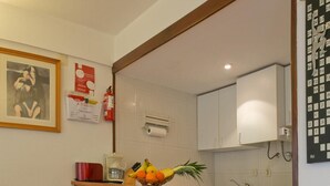 A compact kitchen with wooden cabinets, a washing machine, and a small bar area with stools. - A Torre by Acasadascasas (Mafra)