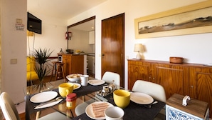 A dining area with a glass table, chairs, and a wooden cabinet with a painting above it. - A Torre by Acasadascasas (Mafra)