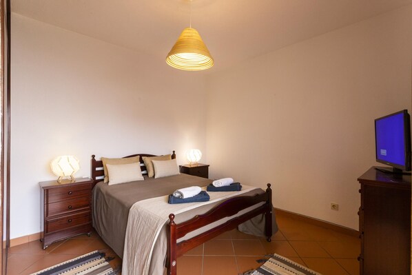 A bedroom with a bed, bedside lamps, a television, and a wooden nightstand.