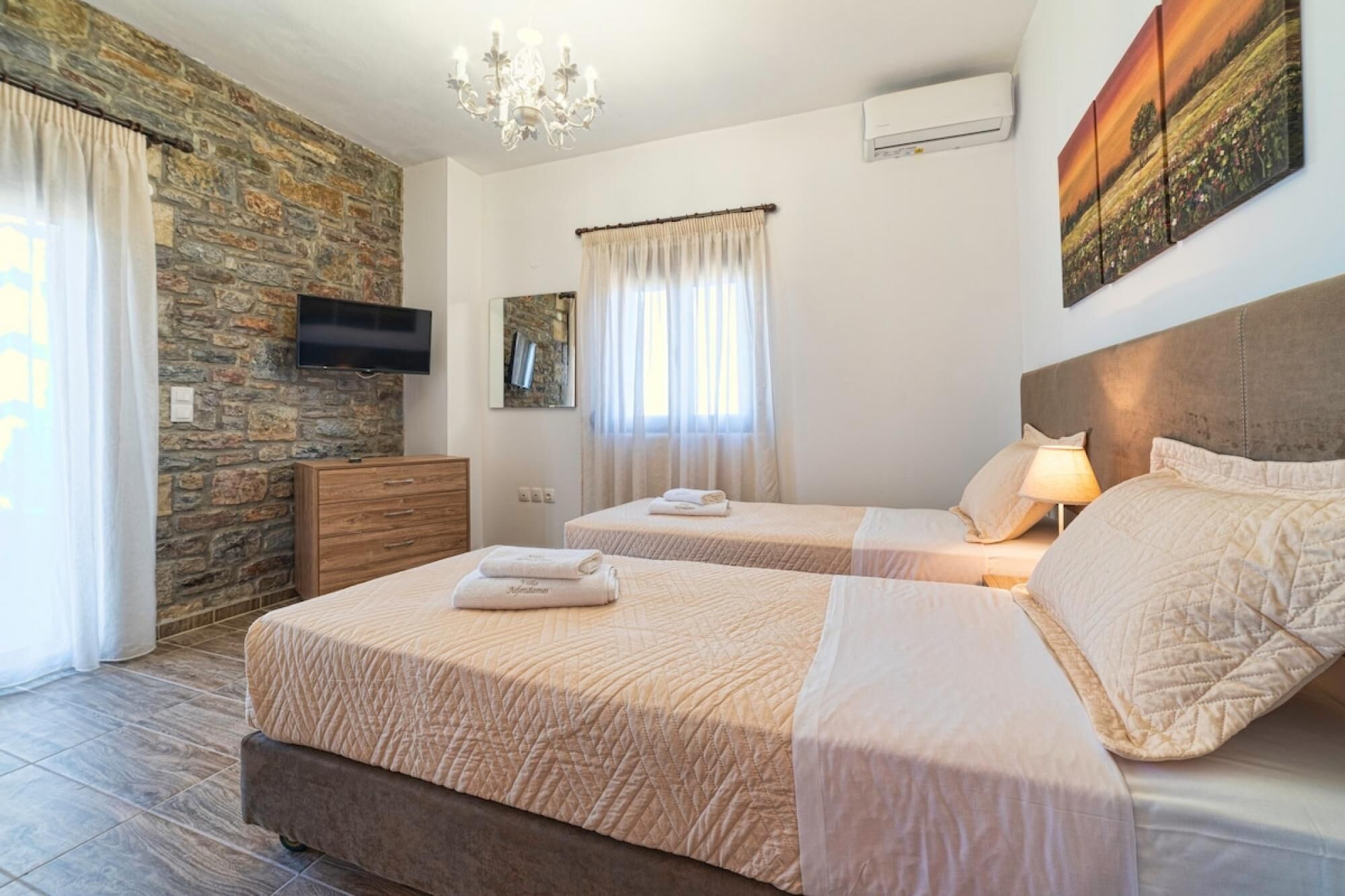 Une chambre d’hôtel avec deux lits, un mur en pierre, un téléviseur à écran plat et un tableau.