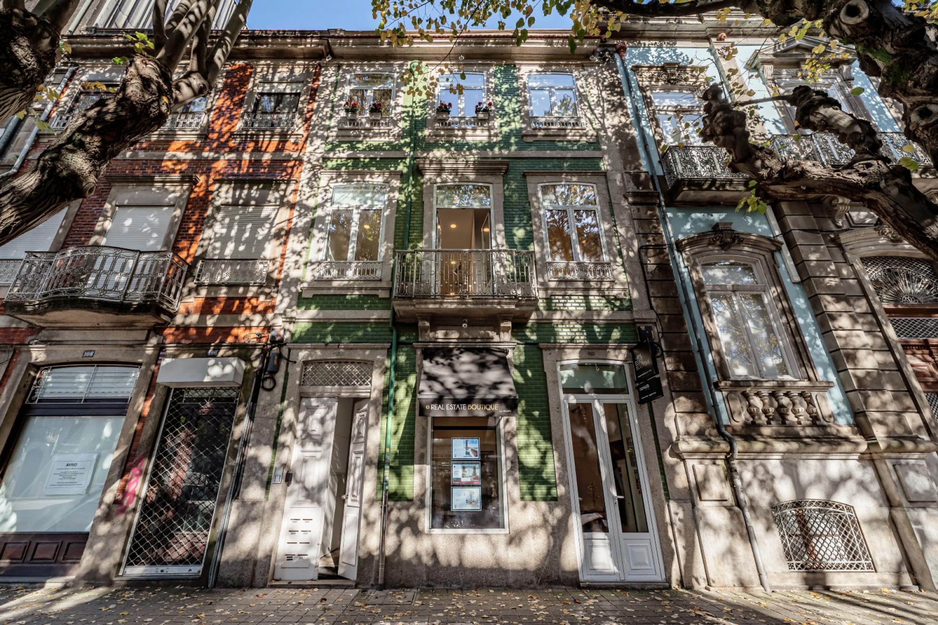 Un edificio storico con numerosi balconi, una facciata verde e un ingresso a livello strada con la scritta 'REAL ESTATE BOUTIQUE'.