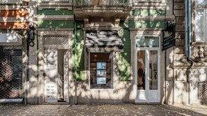 Fachada de edificio con un letrero de una boutique inmobiliaria, una puerta y un cartel en el ventanal.