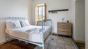Een slaapkamer met een metalen bedframe, witte beddengoed, een houten dressoir en een vloerkleed met een patroon.