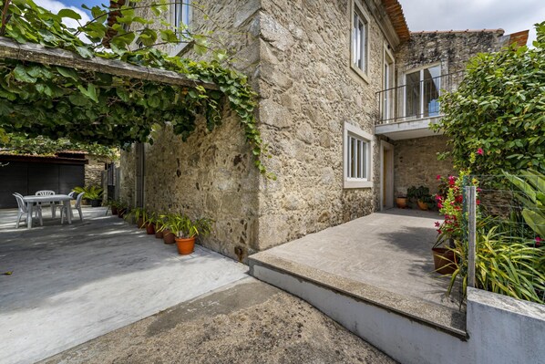 Ein Steinhaus mit Balkon, Blumentöpfen und einer Beton-Terrasse.