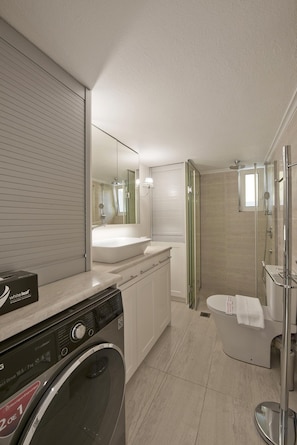 Un baño moderno con lavadora integrada, un espejo grande, zona de ducha y un inodoro.