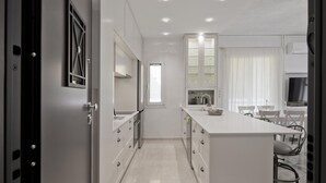 A modern kitchen with white cabinets, a central island, and a dining area with chairs. - Belva Blue in Glifada (Glyfada)