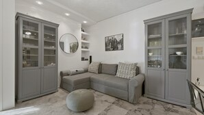 A modern living room with a grey sectional sofa, a round mirror, and grey cabinets with glass doors. - Belva Blue in Glifada (Glyfada)