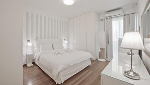 A modern bedroom with a large bed, bedside tables, a glass dresser, and a mirror. - Belva Blue in Glifada (Glyfada)