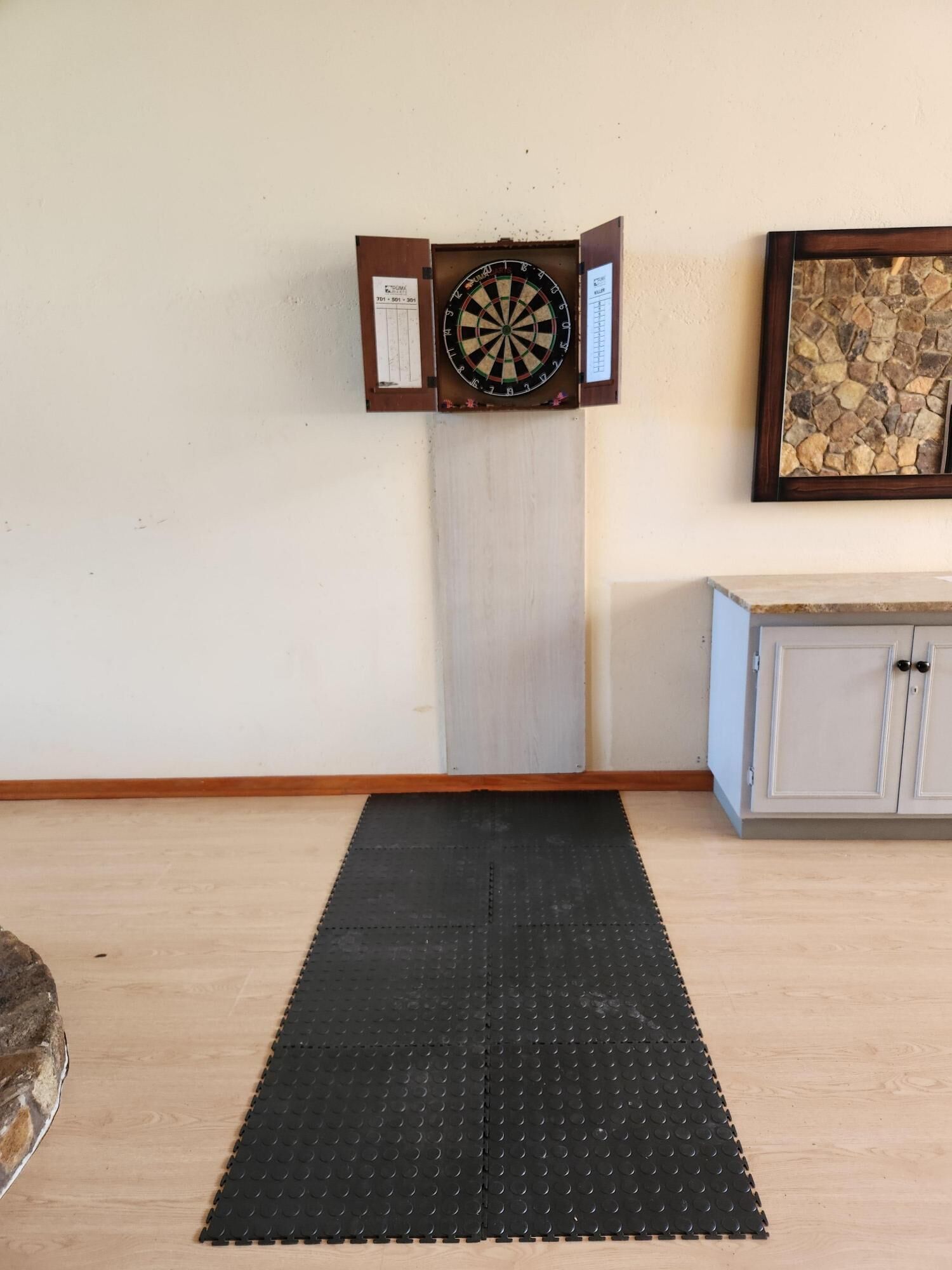 A dartboard mounted on a wall with a black mat in front.