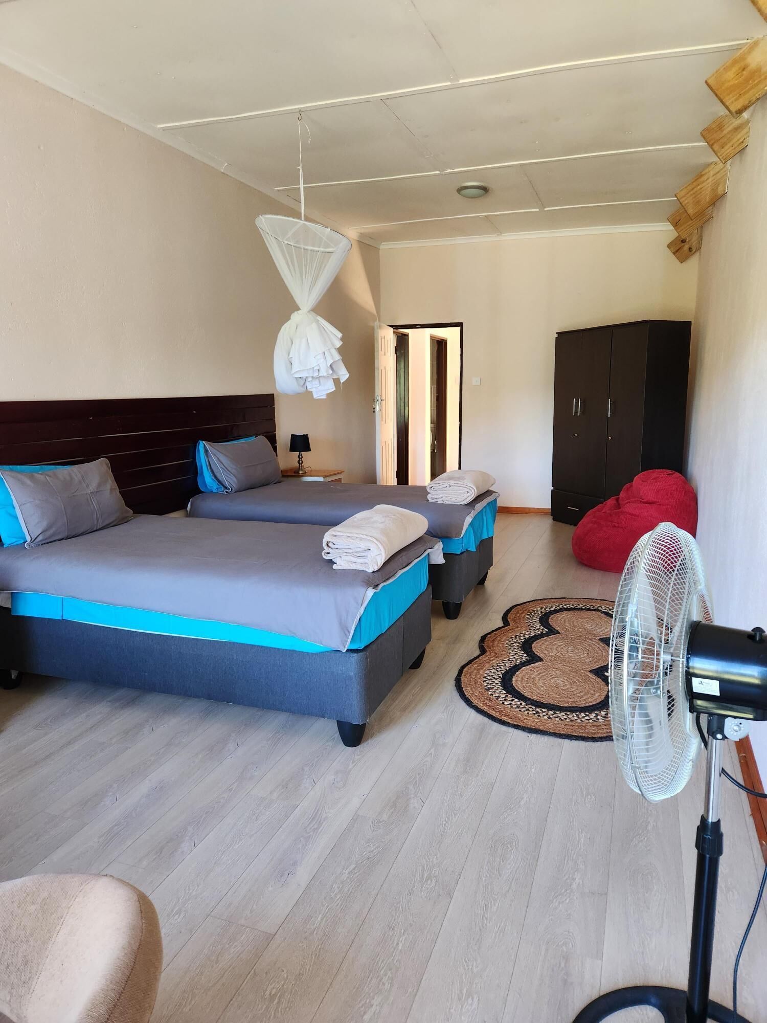 Ein Schlafzimmer mit zwei Betten, einem Standventilator, einem Kleiderschrank und einem roten Sitzsack.