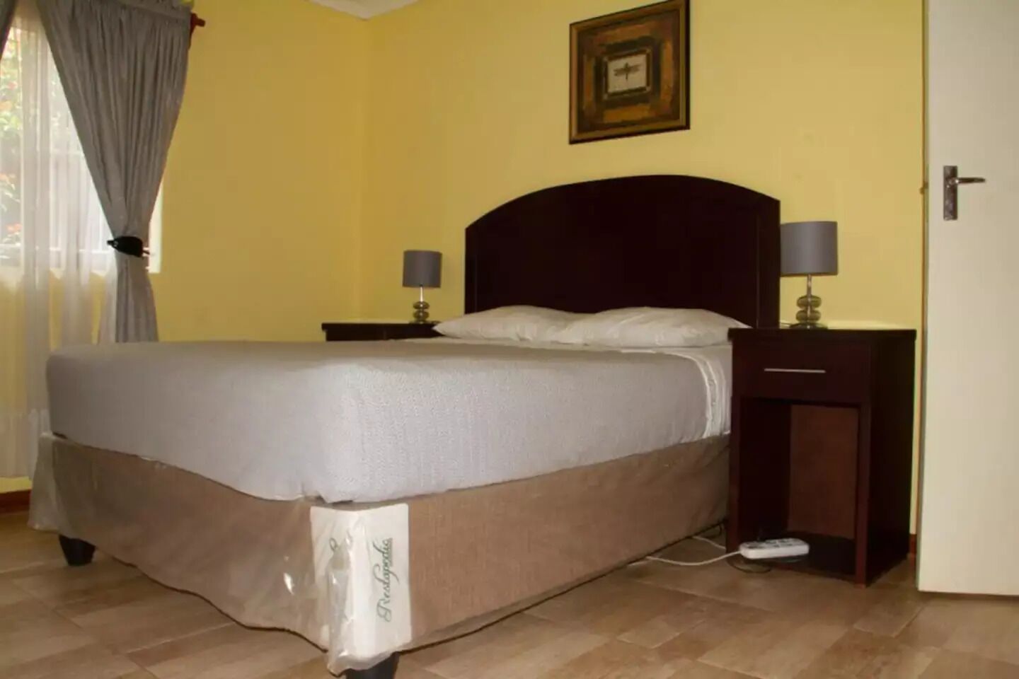 A neatly made bed with a white and brown bedspread, two bedside lamps, a nightstand, and a framed picture on the wall.