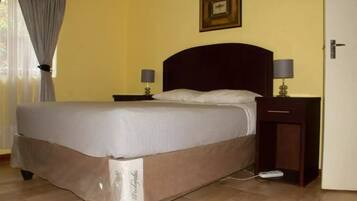 A neatly made bed with a white and brown bedspread, two bedside lamps, a nightstand, and a framed picture on the wall.