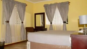 A hotel room with a bed, a chair, a desk, a lamp, and curtains. - Cosy 3 Bedroom Cottage - 2034 (Harare)