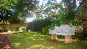 A garden with a stone bench, a brick pathway, and various potted plants. - Cosy 3 Bedroom Cottage - 2034 (Harare)