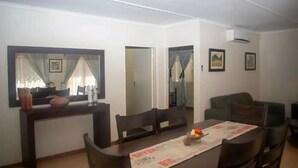 A dining area with a table set for four, a mirror above the table, and a green sofa in the background. - Cosy 3 Bedroom Cottage - 2034 (Harare)
