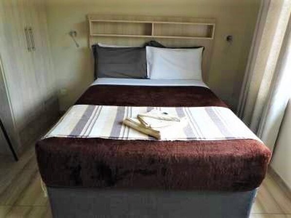 Uma cama de solteiro com cabeceira de madeira, colcha listrada e duas almofadas.