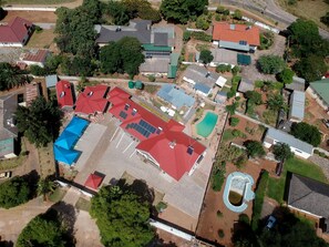 An aerial view of a residential area with multiple houses, a swimming pool, and a large open space with solar panels. - Standard Room in Morningside Guesthouse - 2090 (Bulawayo)