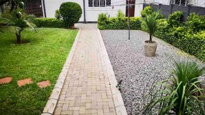 A pathway leading to a building with a white exterior, surrounded by greenery and a gravel area. - Chic Modern House on Neasden - 2085 (Bulawayo)