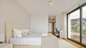 A modern bedroom with a large bed, a walk-in closet, and a balcony with a city view.