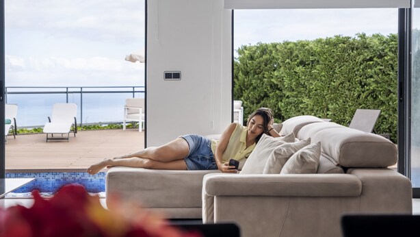 A modern living room with a large window overlooking a pool and a balcony with outdoor furniture.