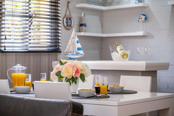 Une table de petit-déjeuner avec un ordinateur portable, une machine à café et un vase de fleurs.