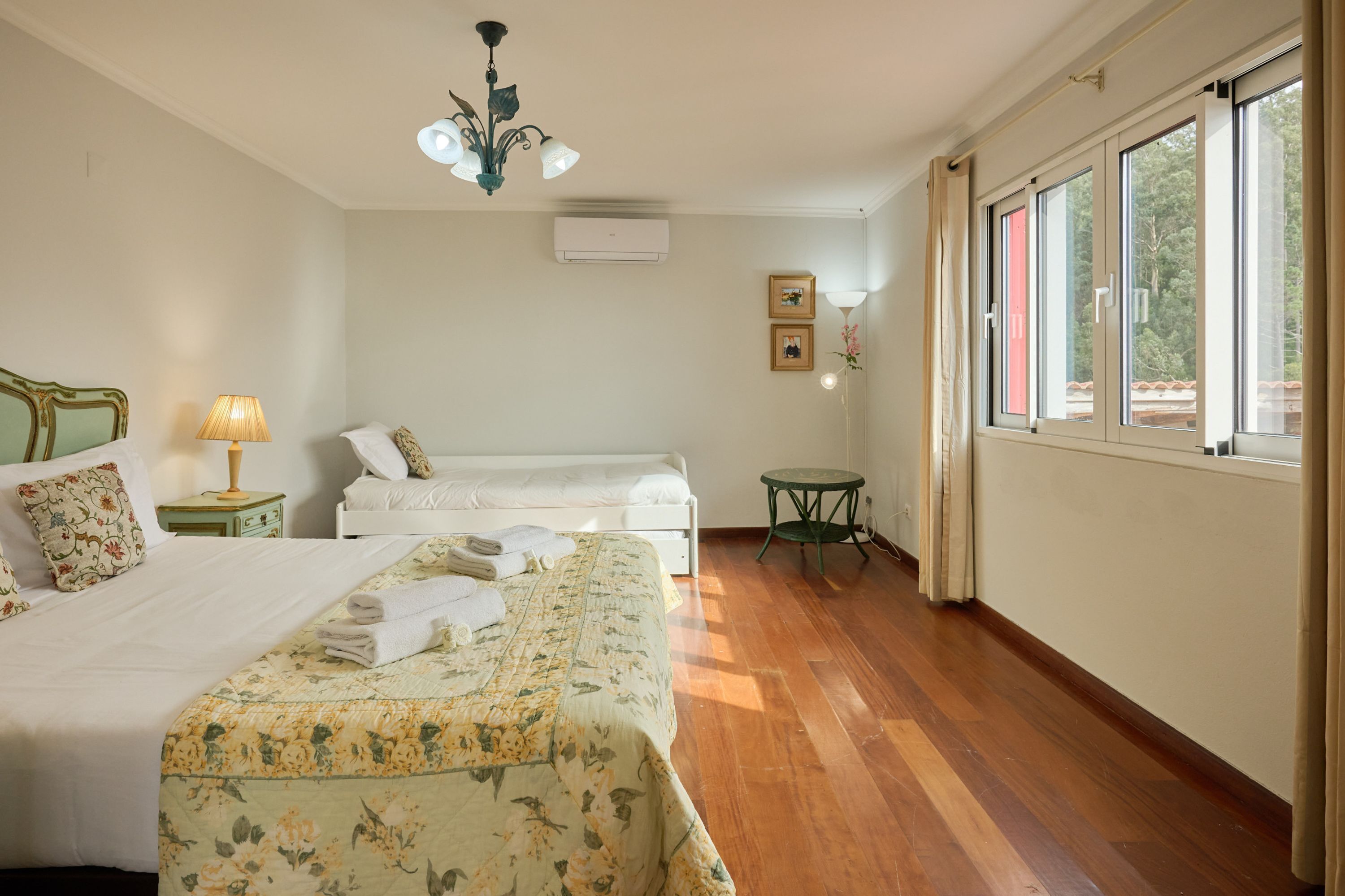 Hotelkamer met een groot bed, een kleiner bed, een ronde tafel en een raam met gordijnen.