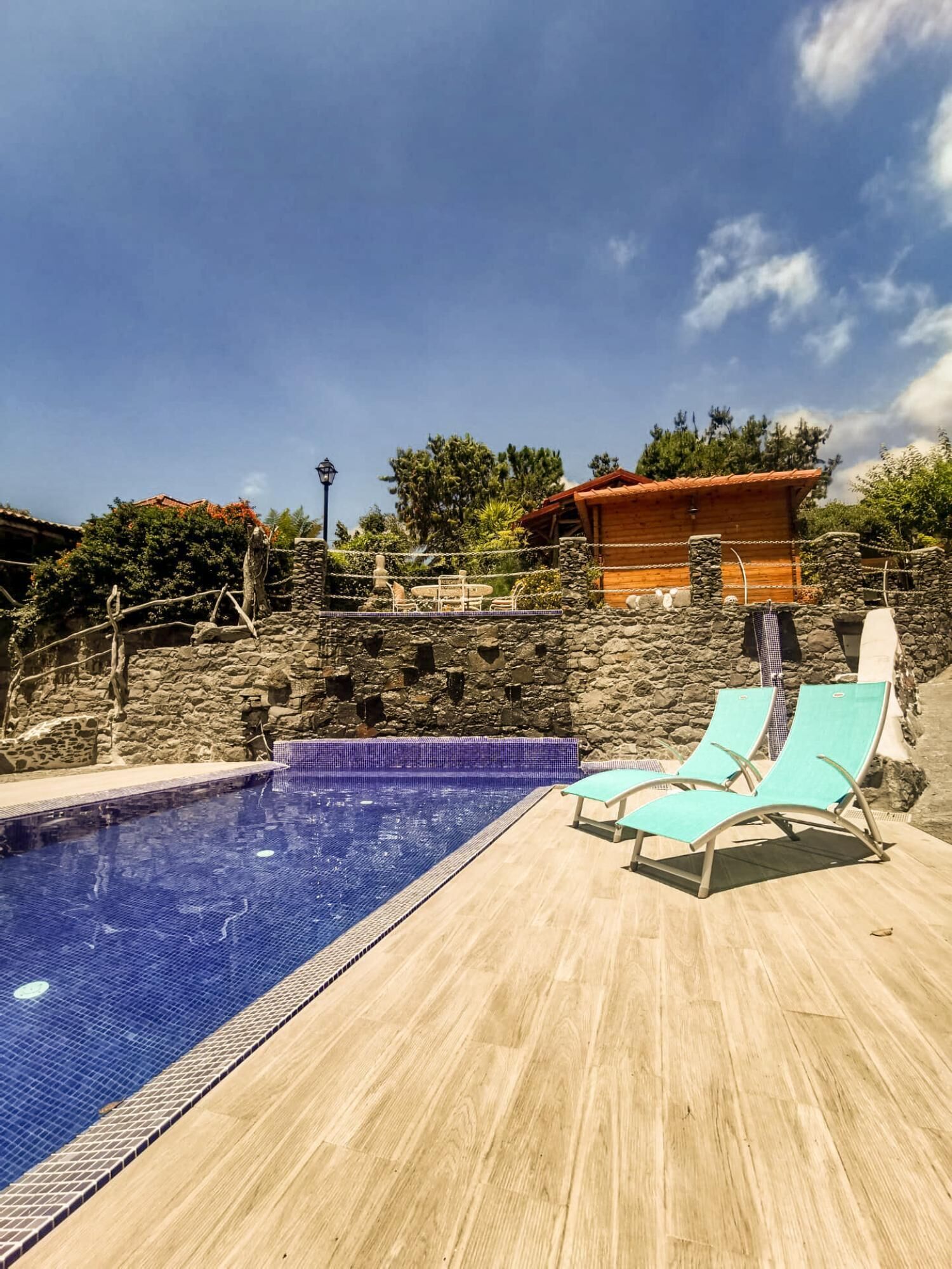 Una piscina con muelle de madera, paredes de piedra y un edificio de madera al fondo.
