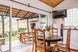 A dining area with wooden furniture, a television, and a kitchen visible through glass doors.