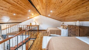 A cozy attic bedroom with wooden ceilings, a staircase, two beds, a dresser, and a lamp. - Ivy Cottage by Homie (Santana)