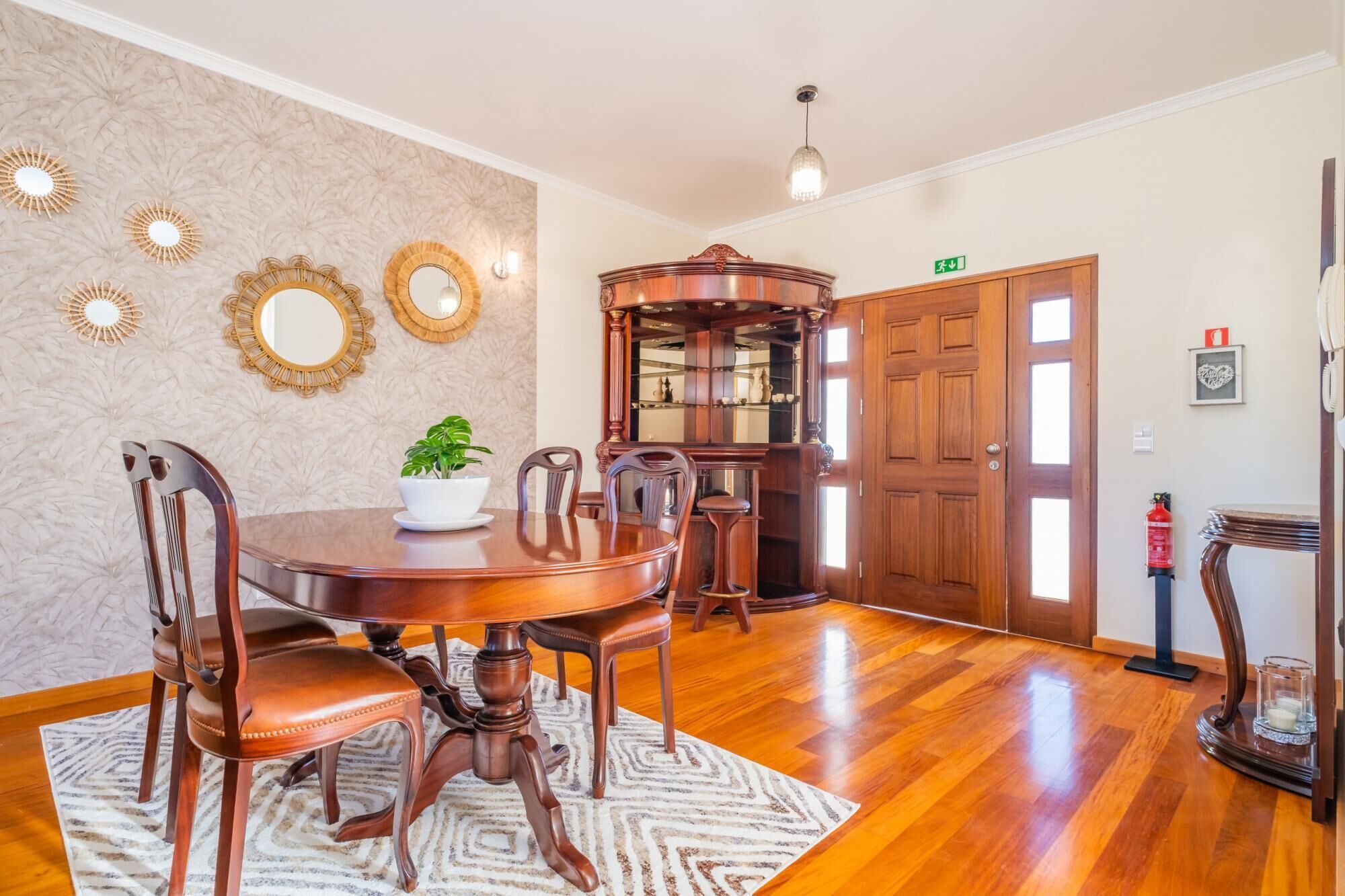 A dining area with a wooden table and chairs, a decorative mirror, and a plant on the table.