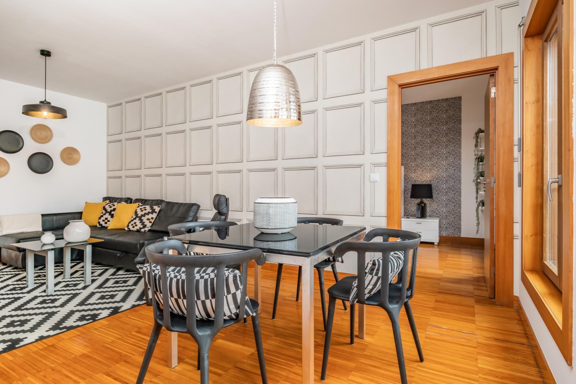 Una sala moderna con sofá, mesa de comedor y sillas, un tapete estampado y una pared decorativa con detalles circulares.
