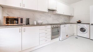Une cuisine moderne avec des meubles blancs, un four à micro-ondes en acier inoxydable, une machine à café, un évier, une cuisinière, un lave-vaisselle et un lave-linge.