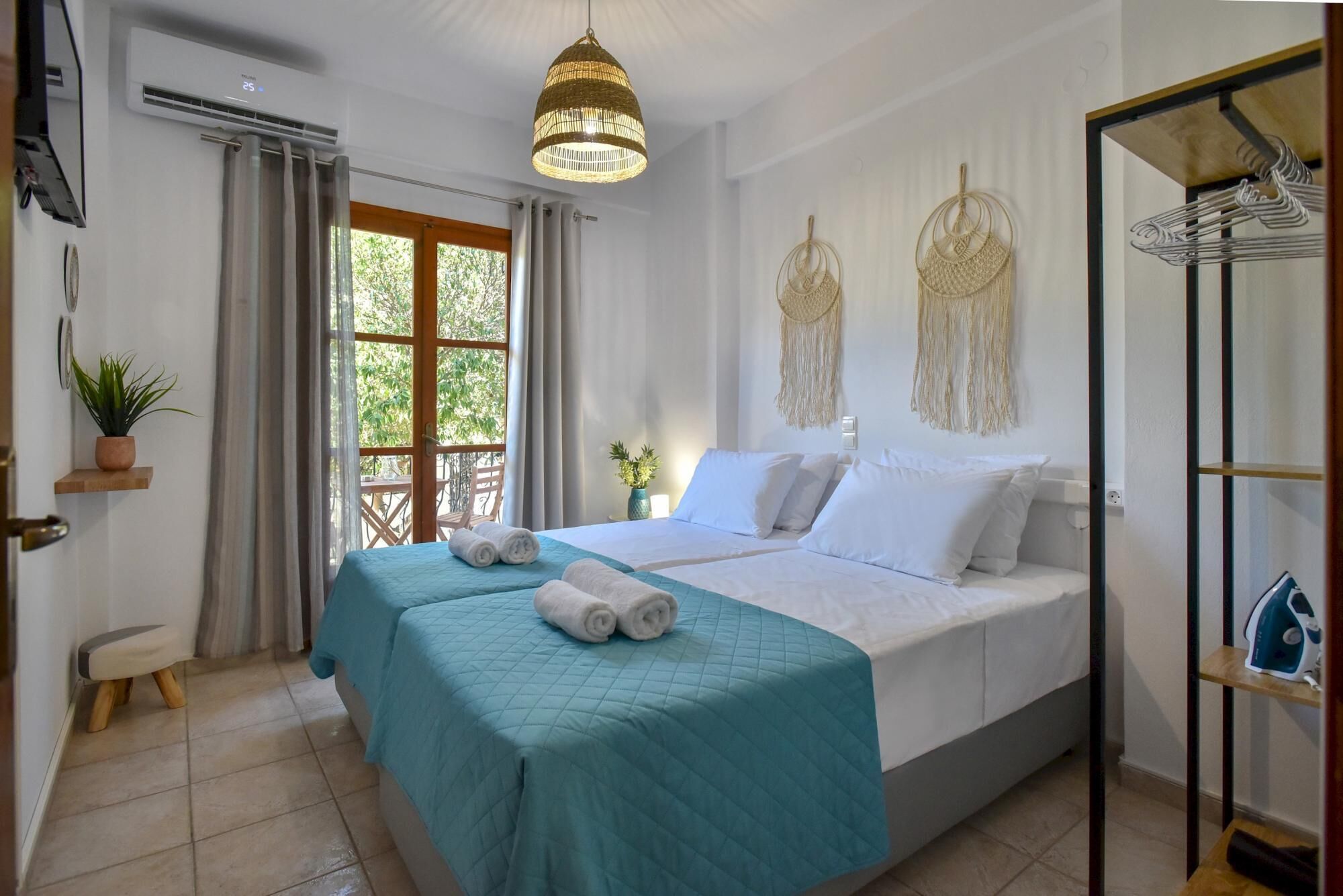 A hotel room with a bed, a hanging light fixture, a plant, and a view of the outdoors.