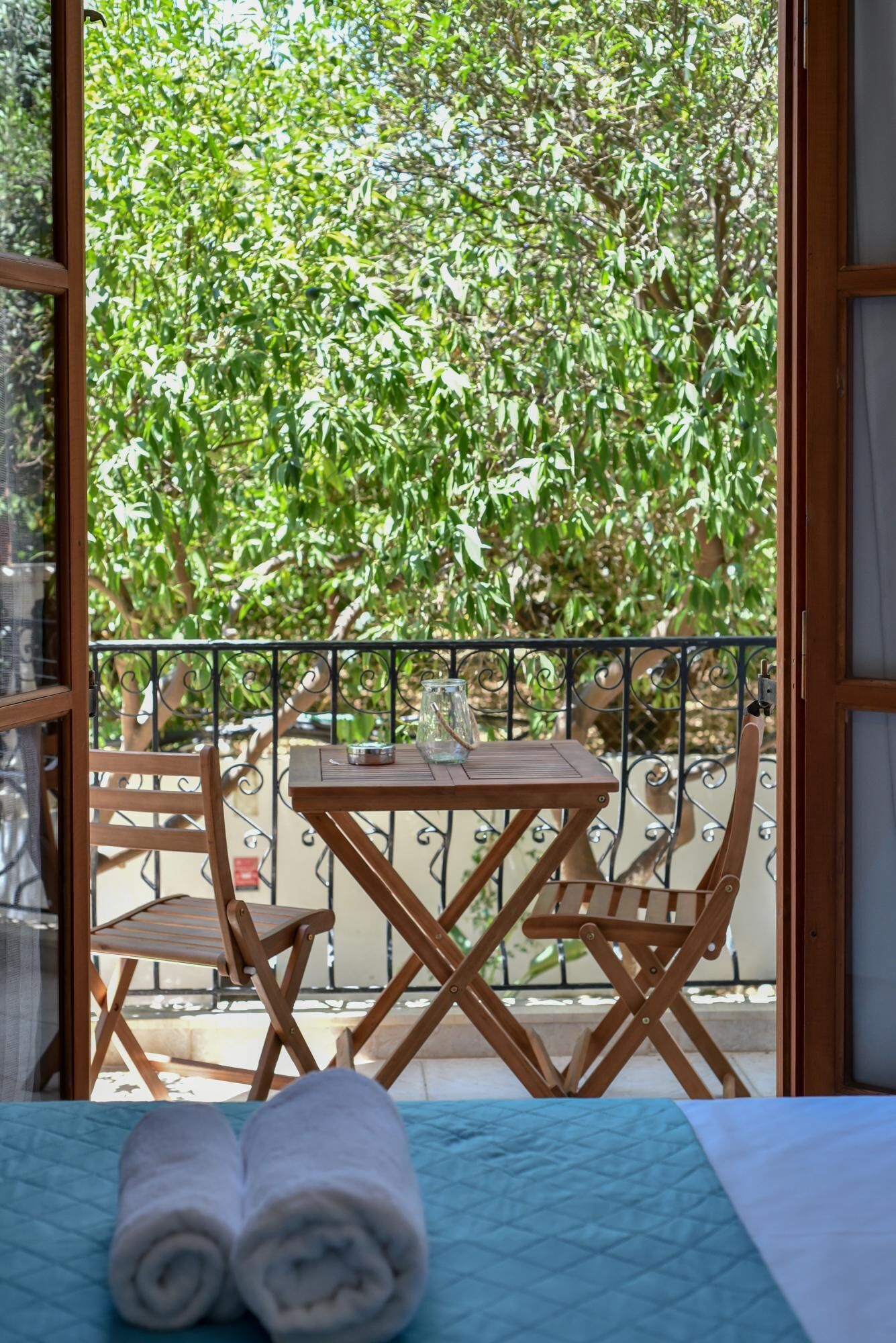 Un balcón con mesa y sillas de madera, barandilla de metal y vistas a follaje verde.