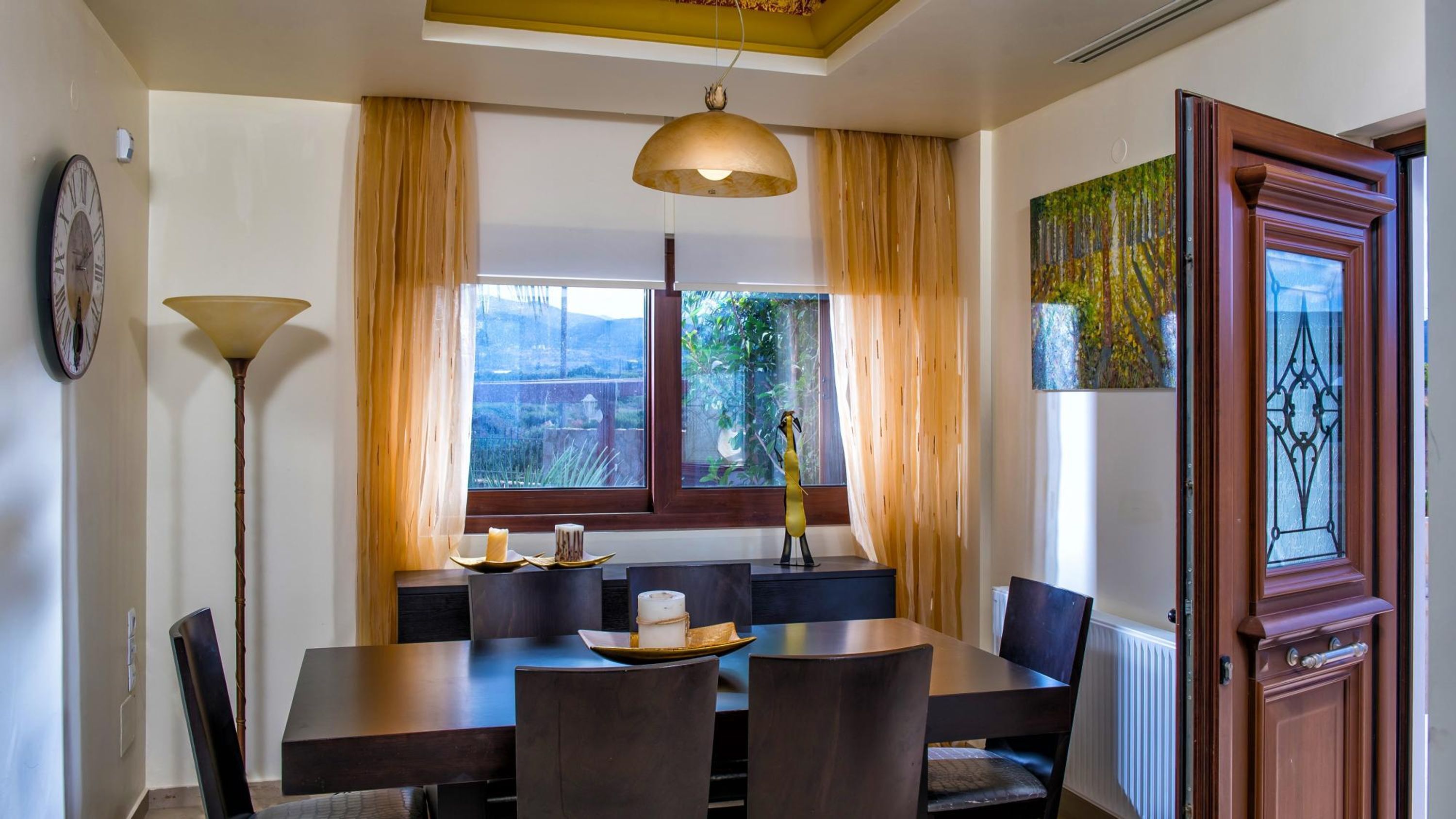 Un coin repas avec une table dressée pour quatre personnes, une horloge au mur et une fenêtre avec des rideaux.