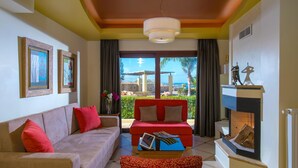 A living room with a sofa, a coffee table, and a fireplace. There are framed pictures on the wall and a view of the outside. - Sunshine Villa (Hersonissos)