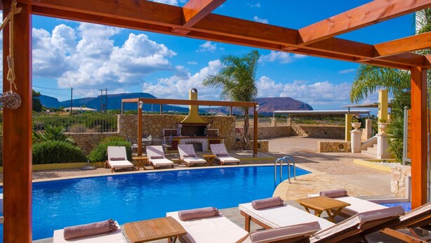 A pool area with lounge chairs and a barbecue under a wooden pergola. - Sunshine Villa (Hersonissos)