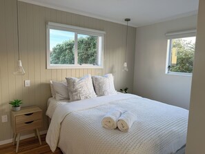 A bedroom with a bed, two bedside tables, a window, and a hanging light fixture.