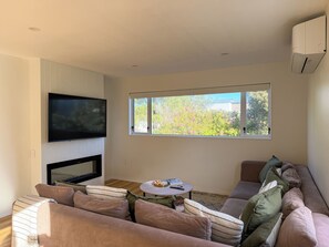 A living room with a flat-screen TV, a fireplace, a sofa, a coffee table, and a window with a view of trees.