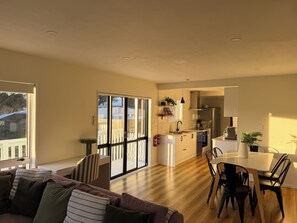 A modern kitchen with a dining area, large windows, and a cozy living room with a sofa and chairs.