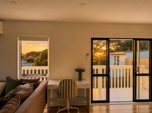 Habitación con sofá, escritorio y una silla. Hay una puerta corrediza de vidrio que da a una terraza al aire libre.