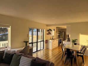 A modern kitchen with a dining area, large windows, and a cozy living room with a sofa and chairs. - Waikanae Beach Abode | Outdoor Bath & Fireplace (Waikanae Beach)