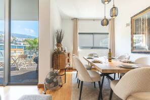A dining area with a table set for two, a wicker side table, and a view of the outdoors. - Funchal Frui Vita by Atlantic Holiday (Funchal)