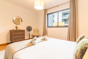 A hotel room with a bed, a chair, a dresser, a fan, and a window with curtains. - Funchal Frui Vita by Atlantic Holiday (Funchal)